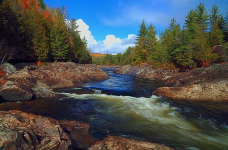 Mountain river in fall forest with red yellow leafs and rocky shore. Mountain river in autumn time. River in Canada.の写真素材