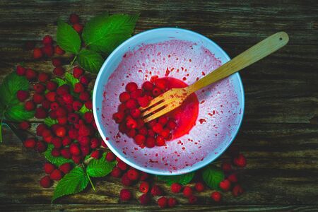 Ripe sweet raspberries in bowl, wooden fork on wooden table. Close up, top view. Red fresh...