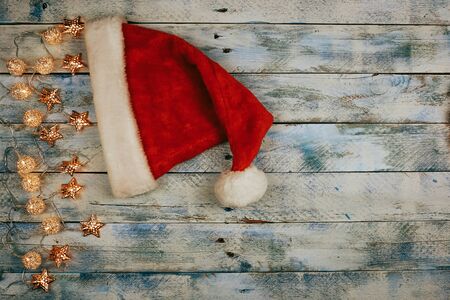Christmas background with santa hat and christmas lights on rustic vintage wooden background. Garland. Flat lay, top view, copy space. Horizontal shot.の写真素材