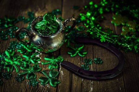 St. Patricks Day composition. Shamrocks, horseshoe, coins, leprechaun hat and silver pot on vintage style wood background. Close up view. Selective focus. Bokeh.の写真素材