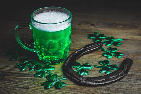 St. Patrick's Day. Green Beer pint with rusty horseshoe on wooden table, decorated with shamrock leaves. Glass of Green beer close-up. Selective focus. Blurred background. の写真素材