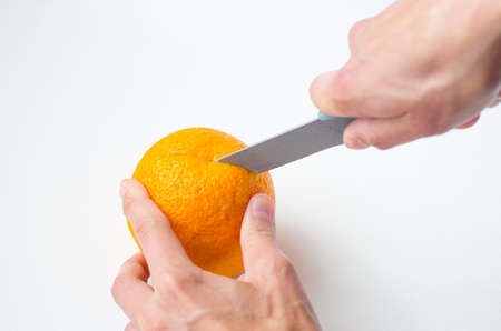 women's hands cut an orange with a knife