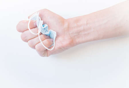 Crush the medical blue disposable mask on a white background with your hand