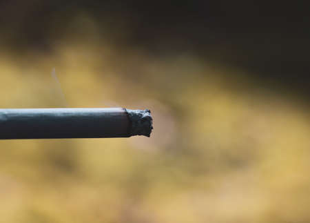 Cigarette with smoke and blurred bokeh as background on a Sunny day, to quit the action of Smoking.の写真素材
