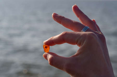a woman's hand with a piece of amber on the background of the sea.の写真素材