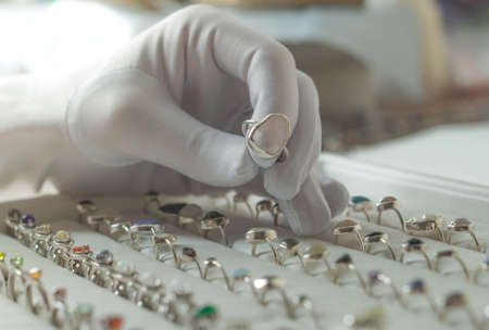 A gloved hand take to ring with gemstones.