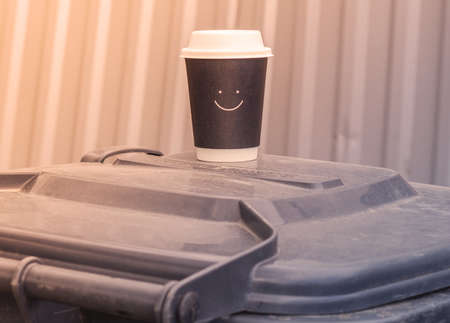 A glass of coffee stands on a trash can. A plastic glass of coffee with a smile.の写真素材