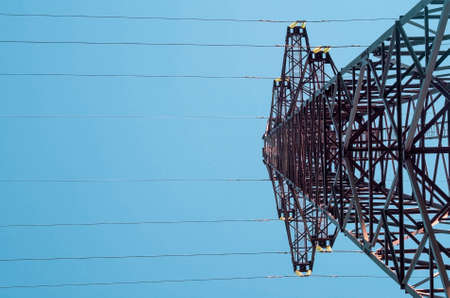 High voltage tower with electricity transmission power lines against blue sky, low angle view.