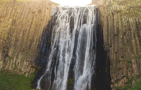 A beautiful waterfall in the mountains. Fresh water flows down from the glacier. Sunset in the...