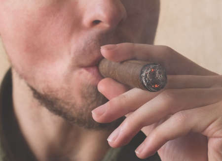 A man smokes a Cuban cigar. Close-up male hands holding a smoking Havana cigarの写真素材