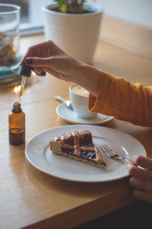 A girl in a yellow jacket is having breakfast in a cafe. Women's hands add THC and CBD oil to cherry pie. The concept of using medical marijuana.の写真素材