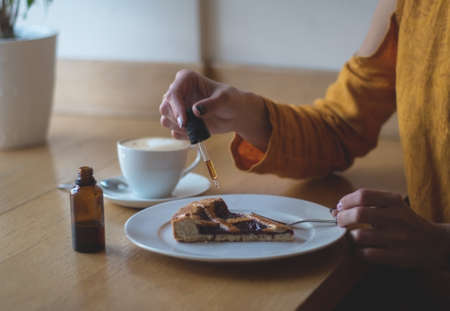 A girl in a yellow jacket is having breakfast in a cafe. Women's hands add THC and CBD oil to cherry pie. The concept of using medical marijuana.の写真素材