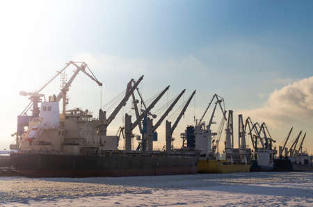 Shipyards on the bay in winter. Cranes, trawlers and ships at sunset on a frosty day.の写真素材