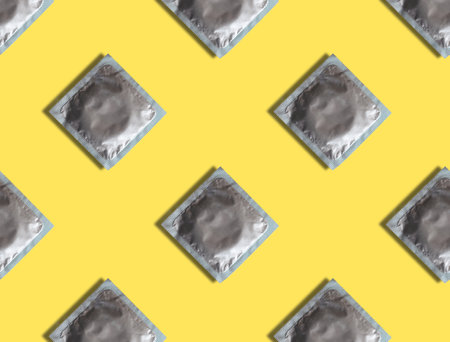 Condoms in a package on a yellow background. Seamless pattern of contraceptives. The concept of safe sex and reproductive health.の写真素材