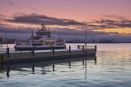 Ferry to Suomenlinna Sveaborg Island from the Market Square of the Finnish capital Helsinki: early morning, pink sunrise, reflection in the water, silhouette of historic buildings on the island.の写真素材