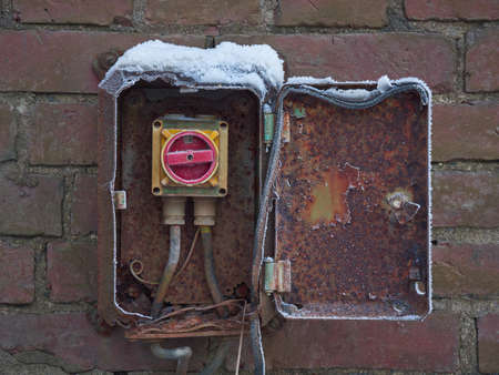 Dangerous Electrical Engineering: old electrical equipment with broken insulation on a brick wall outdoors.の写真素材