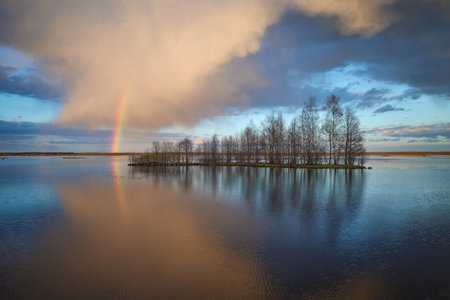 Nature of Northern Europe: lake before sunset, island, rainbow, colorful clouds with reflection, May.の写真素材