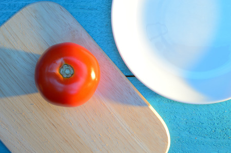 red apple on a wooden board on a blue-turquoise table near a ceramic white plateの写真素材