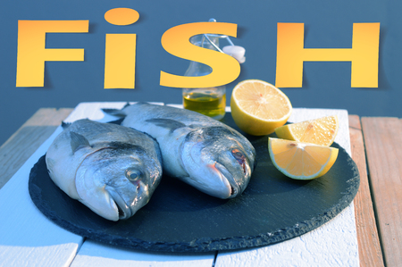 paper cut out style word fish with soft shadows . origami on dorado fish on a black plate with lemon and olive oil bottle backgroundの写真素材