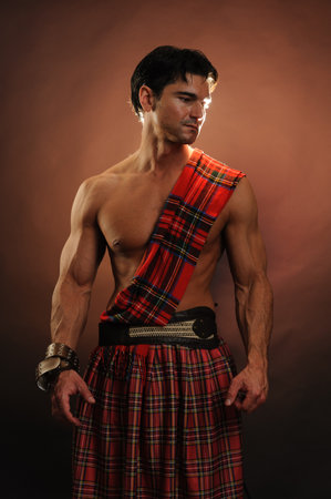 Muscular young man with a red tartan Scottish kilt.