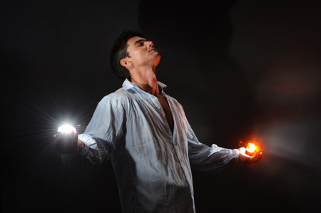 Young man in a shirt with glowing objects in his hands on a black backgroundの写真素材