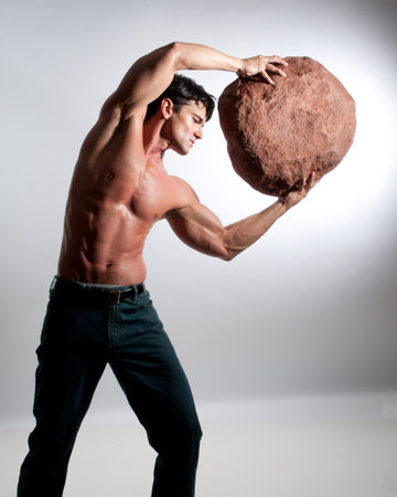 Muscular young man holding a big stone in his hand. Studio shot.の写真素材