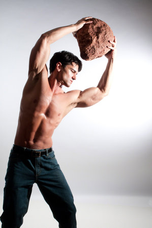 Muscular young man holding a large stone in his hand. Studio shot.の写真素材