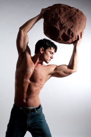 muscular young man holding big rock on grey background, studio shotの写真素材