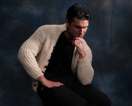 Attractive young man in a beige sweater sitting on a dark backgroundの写真素材