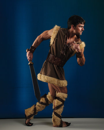 Portrait of a gladiator with sword over blue background. Studio shot.