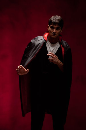 Portrait of a handsome young man in a vampire costume on a red background