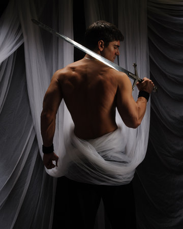 Young man with a sword in his hands on a dark background.