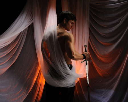 Young man with sword and white cloth on the background of the curtainの写真素材