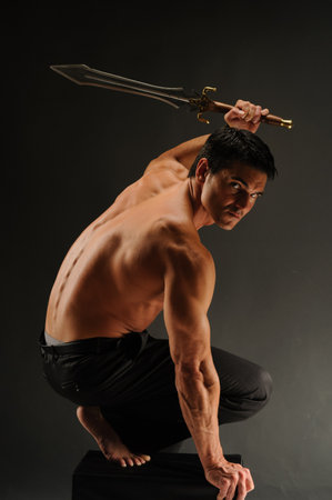 Portrait of a shirtless man with a sword on a black backgroundの写真素材