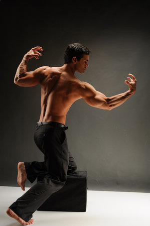 Handsome young man with bare torso in black pants dancing on gray backgroundの写真素材