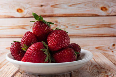 Fresh strawberries on a light wooden table on a plateの写真素材