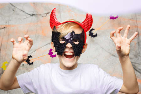 a child with a mask and horns on his head plays with a Halloween pumpkinの写真素材