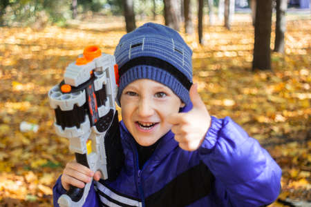 a boy in an autumn Park plays with a toy gun