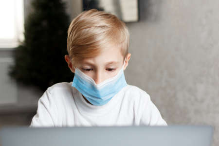 a child in a medical mask with a laptop performs homework for online training
