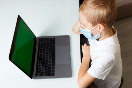 a child in a medical mask with a laptop at home in quarantine training online