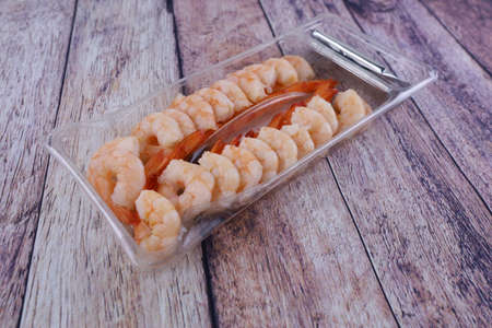 Shrimp peeled and cooked in a plastic container on a wooden table