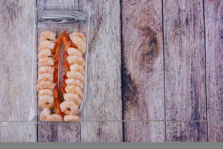 Shrimp peeled and cooked in a plastic container on a wooden tableの写真素材
