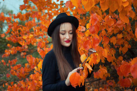 girl with red lipstick in a hat and mask on the background of an autumn tree