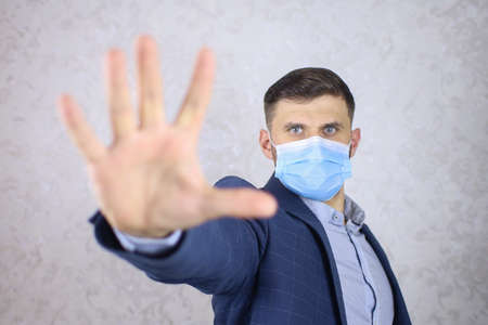 a businessman in a medical mask holds out his hands and makes a stop gesture