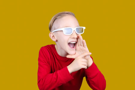 a child in 3D glasses puts his hand to his ear and tries to hear somethingの写真素材
