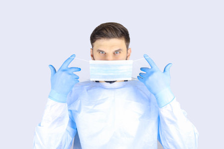 Male doctor in a medical gown, mask and gloves holding a laptopの写真素材