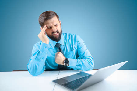a bearded male businessman taps the trackpad behind his laptop with his finger