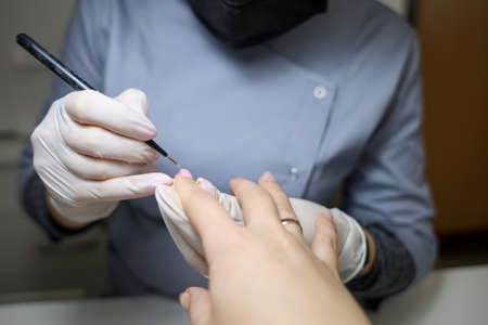 Girl manicure master does nail manicure. A manicurist in a blue shirt and black mask makes the...
