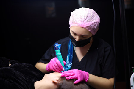 A permanent makeup artist tightens the skin near the eyebrows to perform the tattoo procedure....