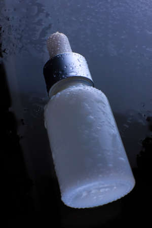On a white bottle with an eyedropper drops of waterの写真素材